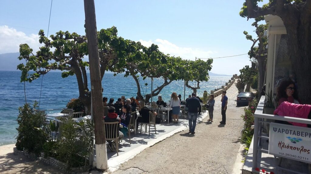 Παραθαλάσσια ψαροταβέρνα με τραπέζια δίπλα στο κύμα και θέα στον Κορινθιακό κόλπο.