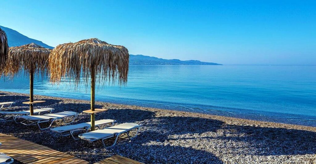 Καλοκαιρινή παραλία στην Καλαμάτα με ήσυχα νερά και ομπρέλες από καλάμι