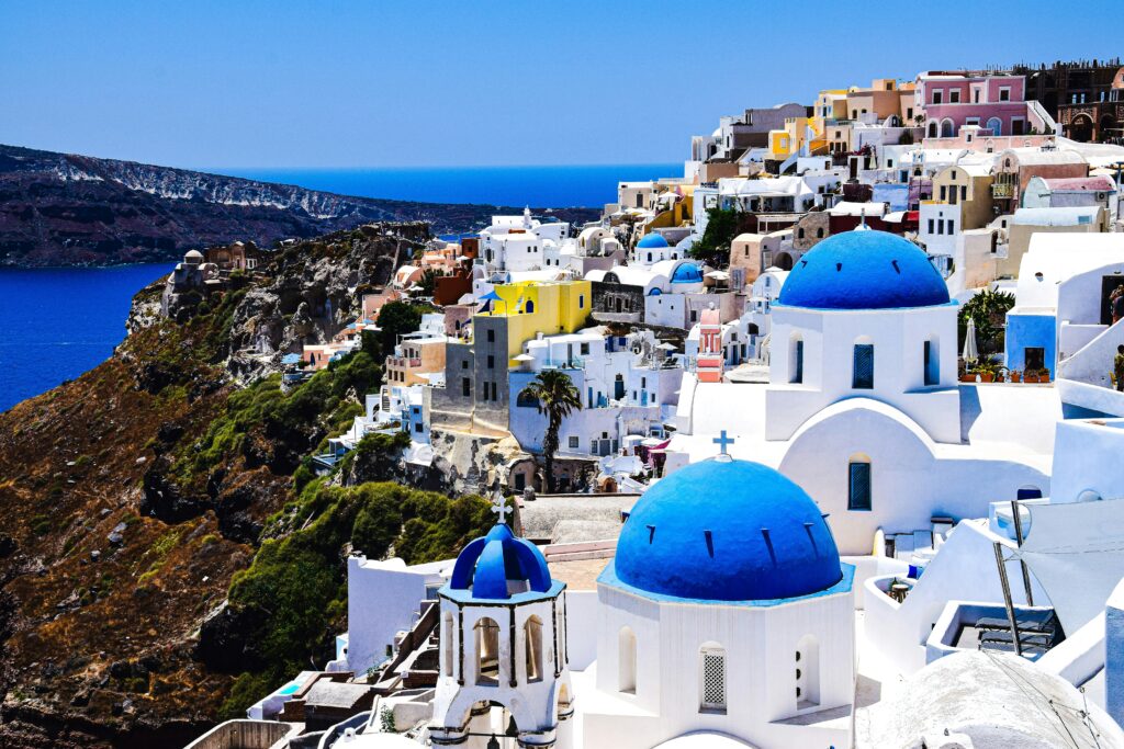 Πανοραμική θέα στην Οία με μπλε τρούλους και γκρεμό πάνω από την Καλντέρα – ταξίδι στη Σαντορίνη