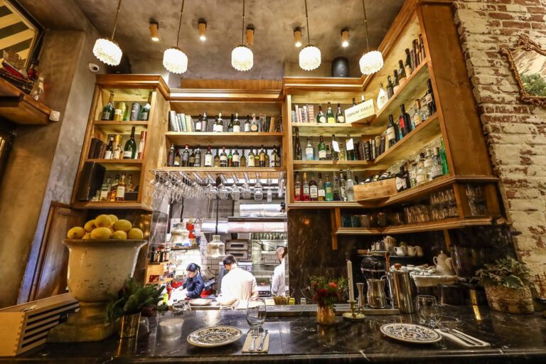 Εσωτερικός χώρος του Yiamas Gastro Bar με ανοιχτή κουζίνα και μπουκάλια σε ξύλινα ράφια