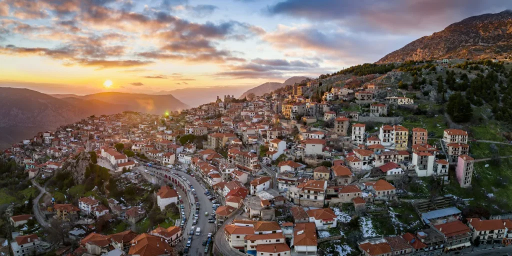 Πανοραμική θέα της Αράχωβας στο ηλιοβασίλεμα με τα πέτρινα σπίτια και τα βουνά του Παρνασσού
